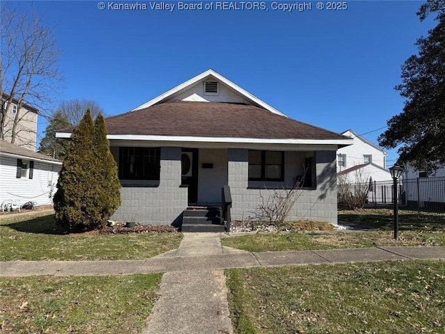 bungalow with a shingled roof, fence, concrete block siding, and a front lawn