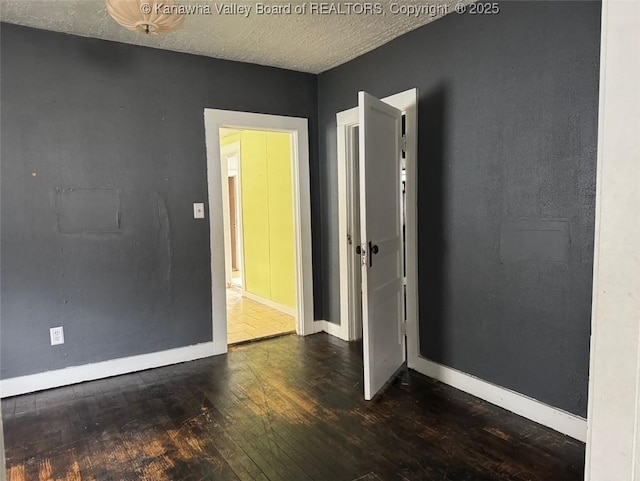 spare room featuring a textured ceiling, wood-type flooring, and baseboards