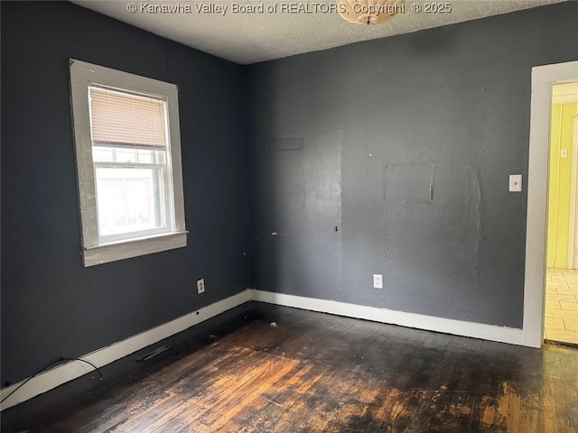 empty room featuring baseboards, a textured ceiling, and hardwood / wood-style floors