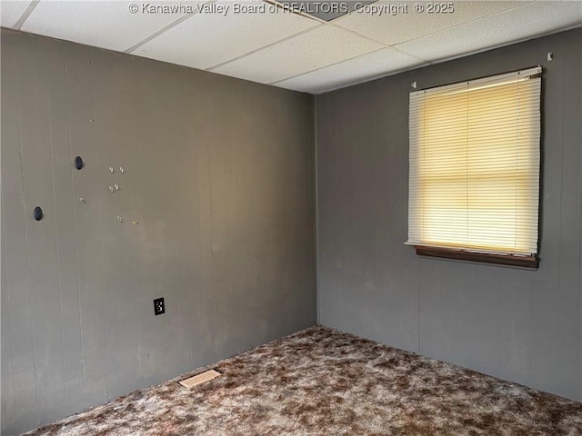 spare room with carpet floors, a drop ceiling, wood walls, and visible vents