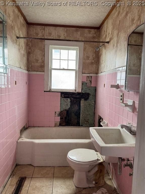 bathroom with a bathtub, tile walls, a textured ceiling, and toilet