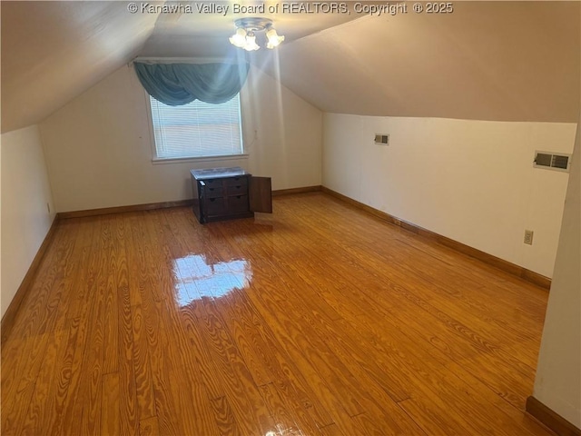 additional living space with lofted ceiling, visible vents, baseboards, and wood finished floors