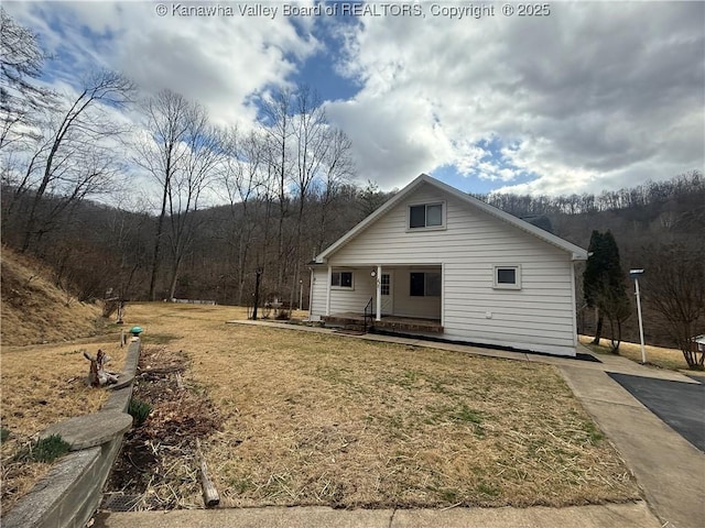 view of front of home with covered porch, a forest view, and a front yard