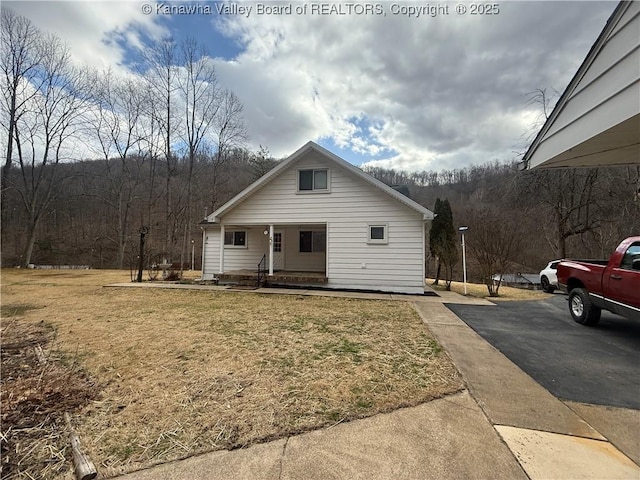 bungalow-style home with covered porch, driveway, a view of trees, and a front lawn