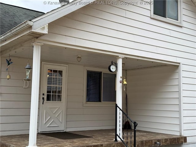 doorway to property featuring a porch and roof with shingles