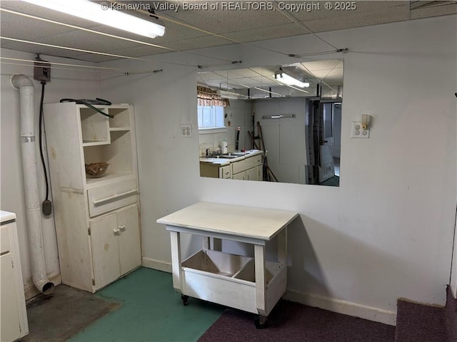 interior space featuring finished concrete flooring, open shelves, light countertops, a drop ceiling, and baseboards