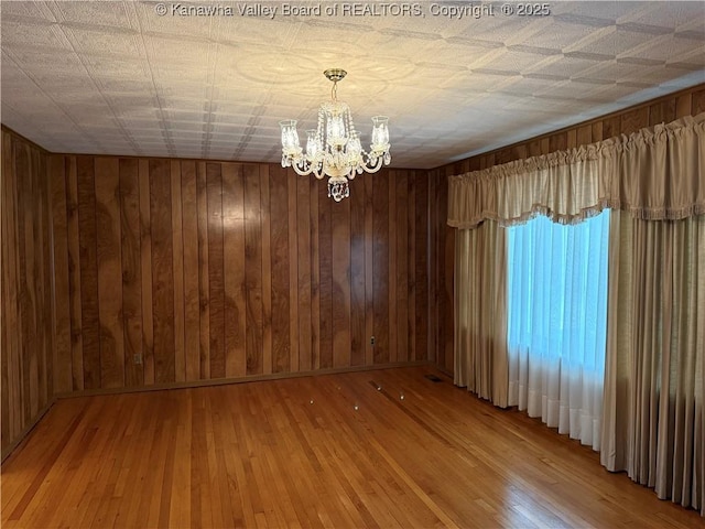 empty room featuring light wood-type flooring, an inviting chandelier, and wood walls