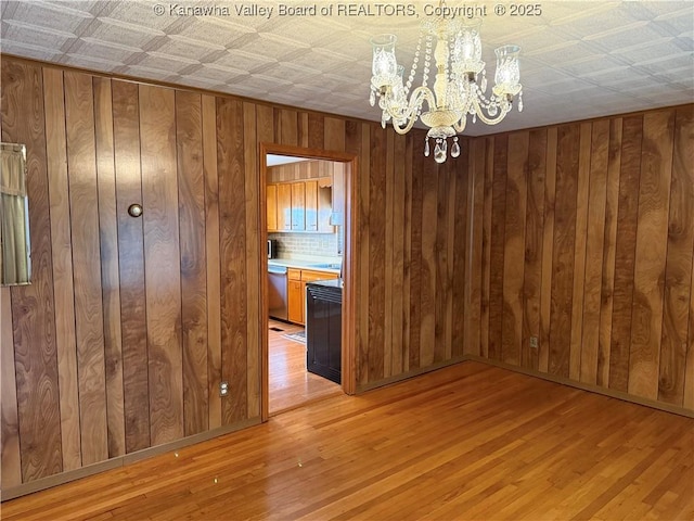 unfurnished dining area featuring a notable chandelier, wood walls, and light wood finished floors