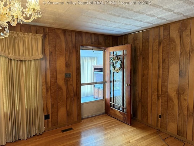 unfurnished room with light wood-type flooring, visible vents, wood walls, and an inviting chandelier