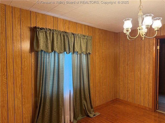 unfurnished room featuring wood walls, a notable chandelier, and wood finished floors