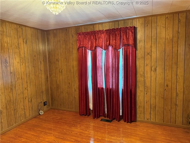 empty room featuring wooden walls, wood finished floors, visible vents, and baseboards