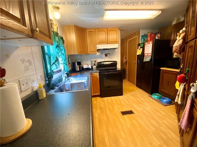 kitchen featuring under cabinet range hood, a sink, visible vents, black appliances, and light wood finished floors