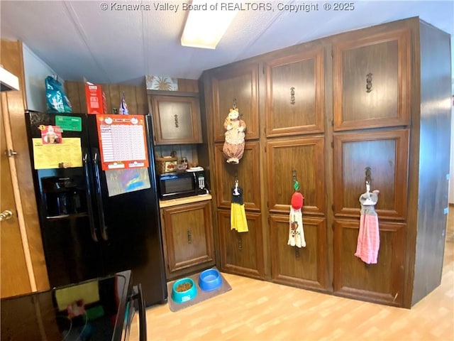 kitchen with brown cabinetry, light countertops, black appliances, and wood finished floors