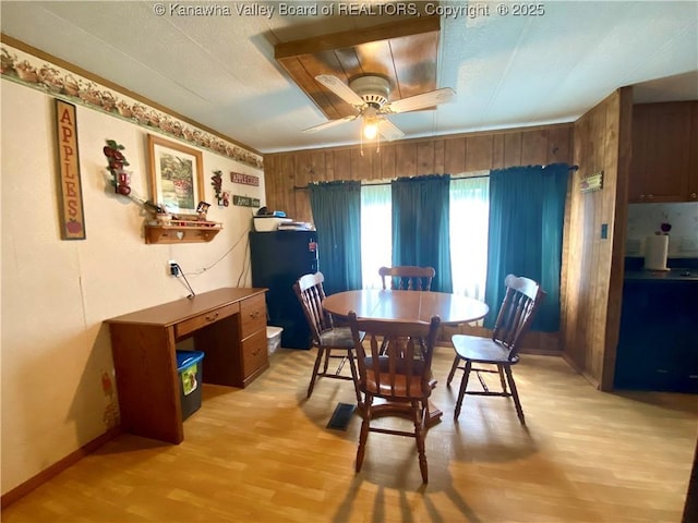 dining room with light wood-type flooring, wood walls, ceiling fan, and baseboards