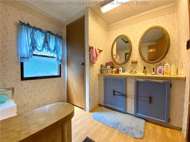 bathroom with ornamental molding, wood finished floors, and wallpapered walls