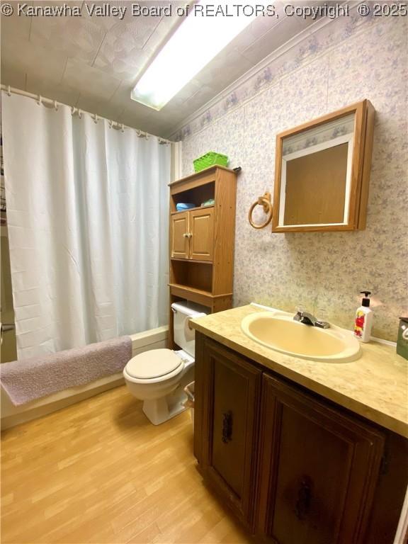 full bath featuring shower / tub combo with curtain, toilet, vanity, wood finished floors, and wallpapered walls