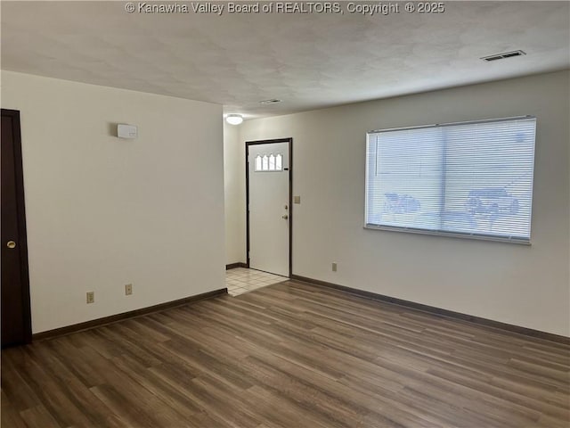 empty room featuring visible vents, baseboards, and wood finished floors