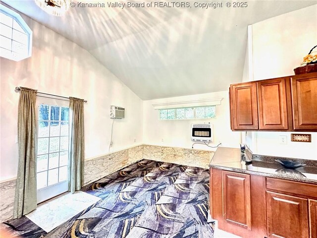 kitchen with lofted ceiling, an AC wall unit, dark stone counters, and heating unit