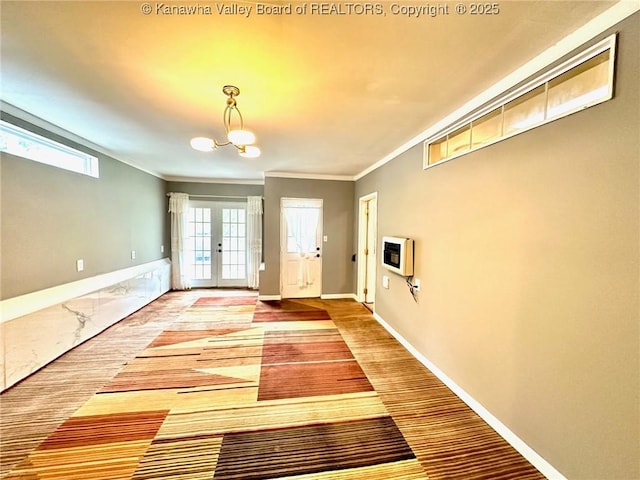 entryway with french doors, crown molding, heating unit, an inviting chandelier, and baseboards