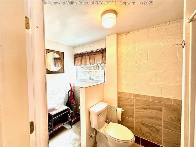bathroom featuring concrete block wall and toilet