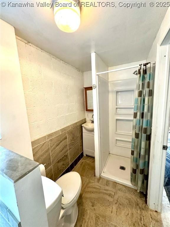 full bath with a stall shower, tile walls, vanity, and toilet