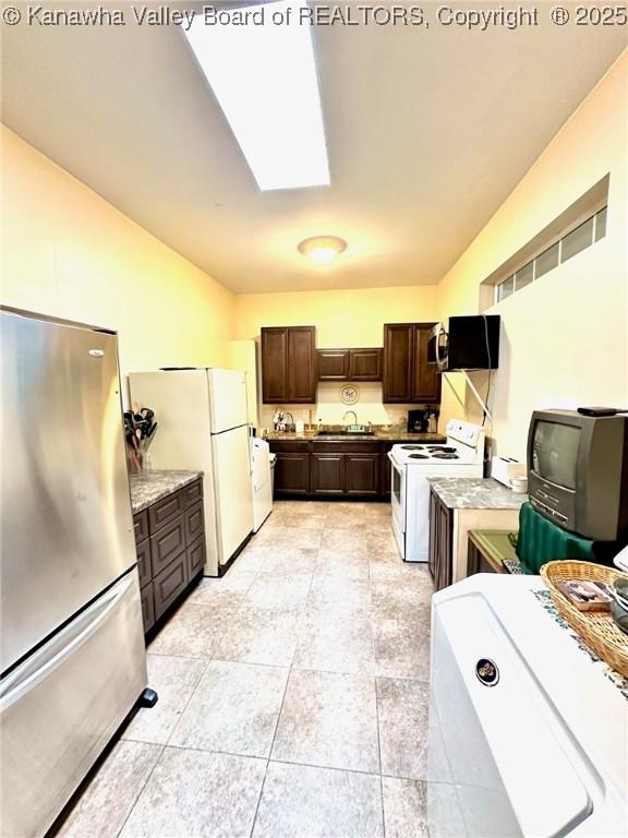 kitchen featuring dark brown cabinets, white appliances, vaulted ceiling with skylight, and a sink
