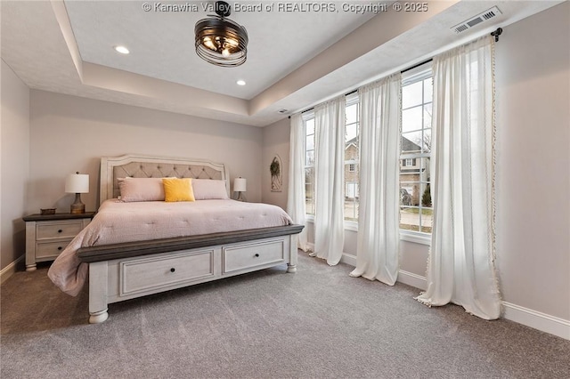 bedroom featuring a tray ceiling, carpet flooring, visible vents, and baseboards