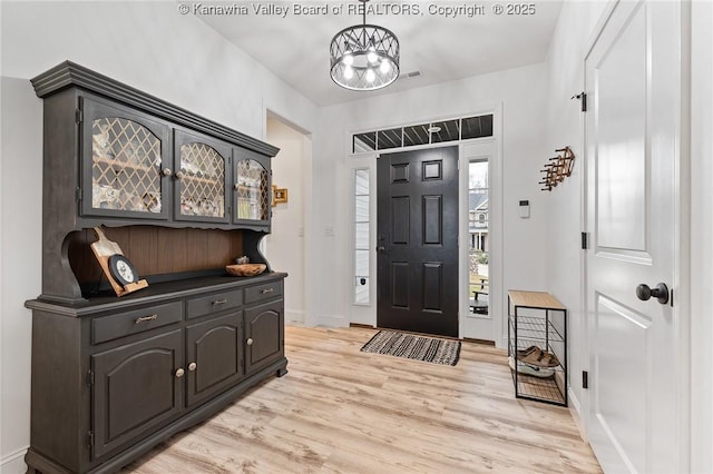 entryway with light wood-style floors, a chandelier, and baseboards