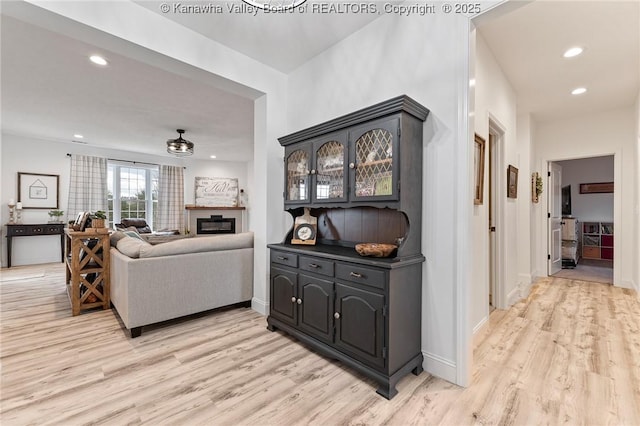 living area featuring light wood-type flooring, a glass covered fireplace, baseboards, and recessed lighting