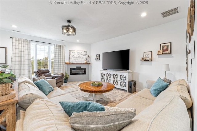 living area with baseboards, visible vents, a glass covered fireplace, wood finished floors, and recessed lighting