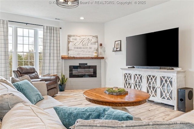 living room with wood finished floors, a glass covered fireplace, visible vents, and recessed lighting