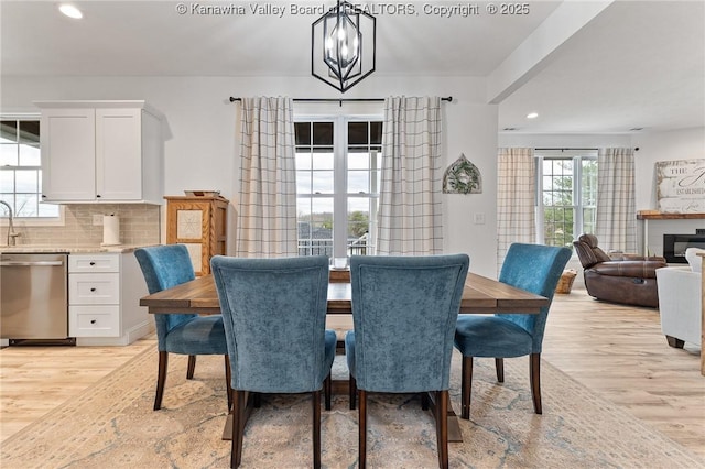 dining room with light wood-style floors, a chandelier, a glass covered fireplace, and recessed lighting