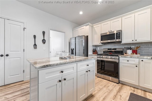 kitchen with light stone counters, white cabinetry, appliances with stainless steel finishes, light wood-type flooring, and tasteful backsplash