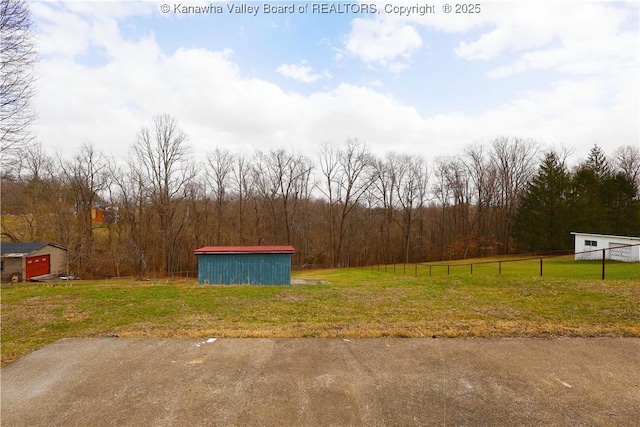 view of yard with an outbuilding, fence, and a view of trees