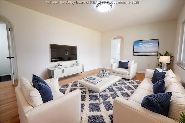 living area featuring arched walkways, baseboards, and wood finished floors