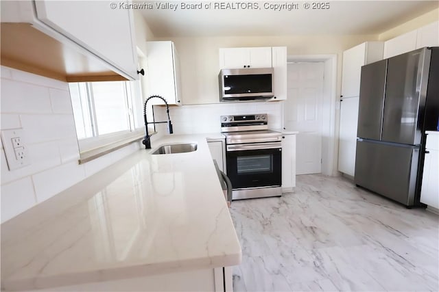 kitchen featuring stainless steel appliances, a sink, white cabinets, marble finish floor, and decorative backsplash