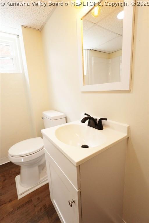 half bathroom featuring a textured ceiling, toilet, a paneled ceiling, wood finished floors, and vanity