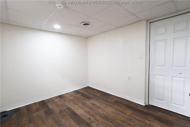 spare room featuring a paneled ceiling, baseboards, visible vents, and dark wood-type flooring