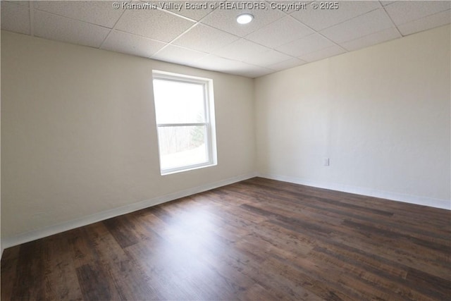 spare room with dark wood-type flooring, a paneled ceiling, and baseboards