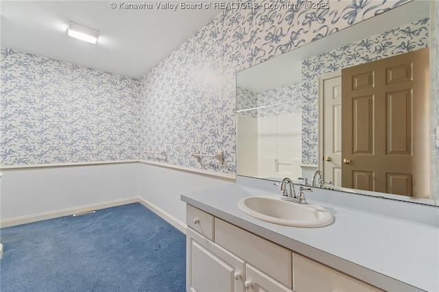 bathroom featuring wallpapered walls, baseboards, a shower, and vanity