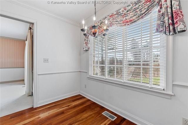 unfurnished dining area with visible vents, baseboards, wood finished floors, crown molding, and a notable chandelier