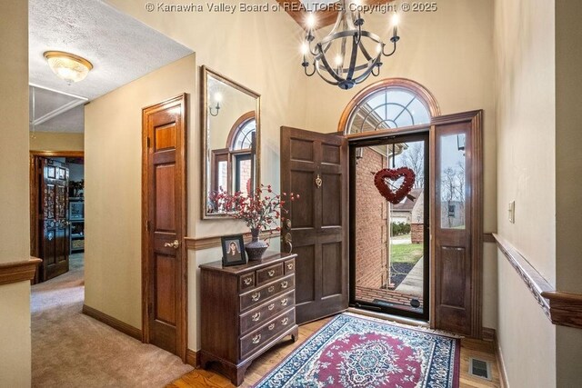 foyer with baseboards, a textured ceiling, visible vents, and a notable chandelier