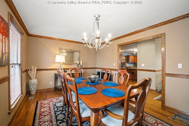 dining room featuring an inviting chandelier, wood finished floors, visible vents, and crown molding