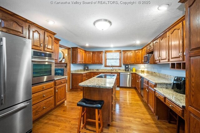 kitchen featuring light stone counters, brown cabinets, a center island, stainless steel appliances, and light wood-type flooring