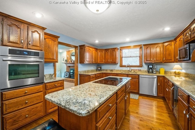 kitchen featuring light stone counters, brown cabinets, stainless steel appliances, a kitchen island, and light wood-type flooring