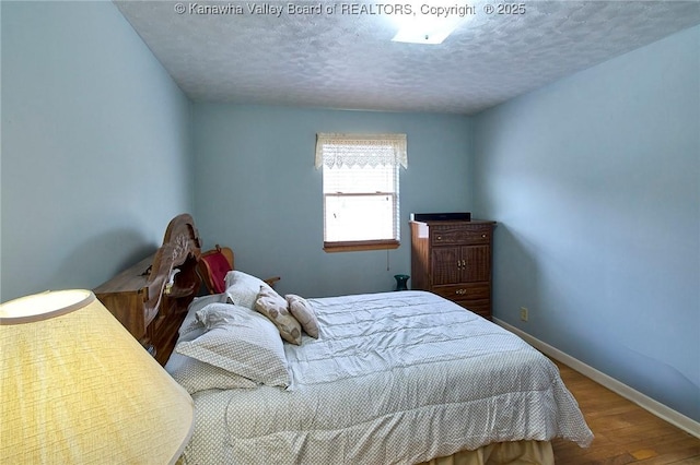 bedroom with a textured ceiling, wood finished floors, and baseboards