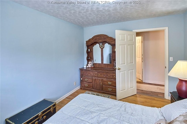 bedroom with a textured ceiling, baseboards, and wood finished floors