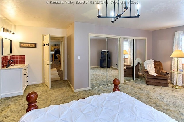 bedroom featuring a closet, light colored carpet, an inviting chandelier, a sink, and baseboards