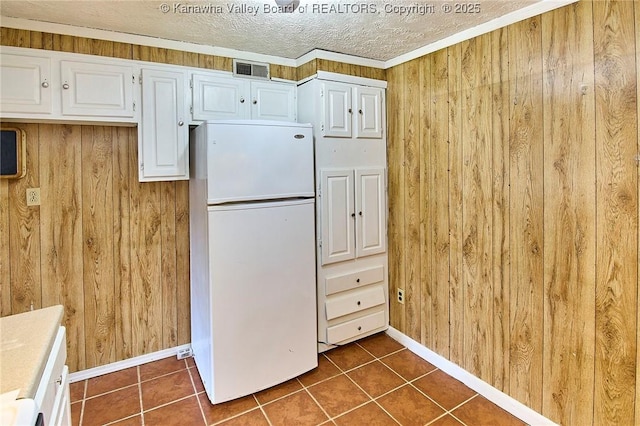 kitchen with freestanding refrigerator, white cabinets, wood walls, a textured ceiling, and dark tile patterned floors