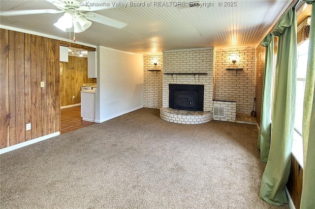 unfurnished living room featuring carpet flooring, a fireplace, wooden walls, and ceiling fan